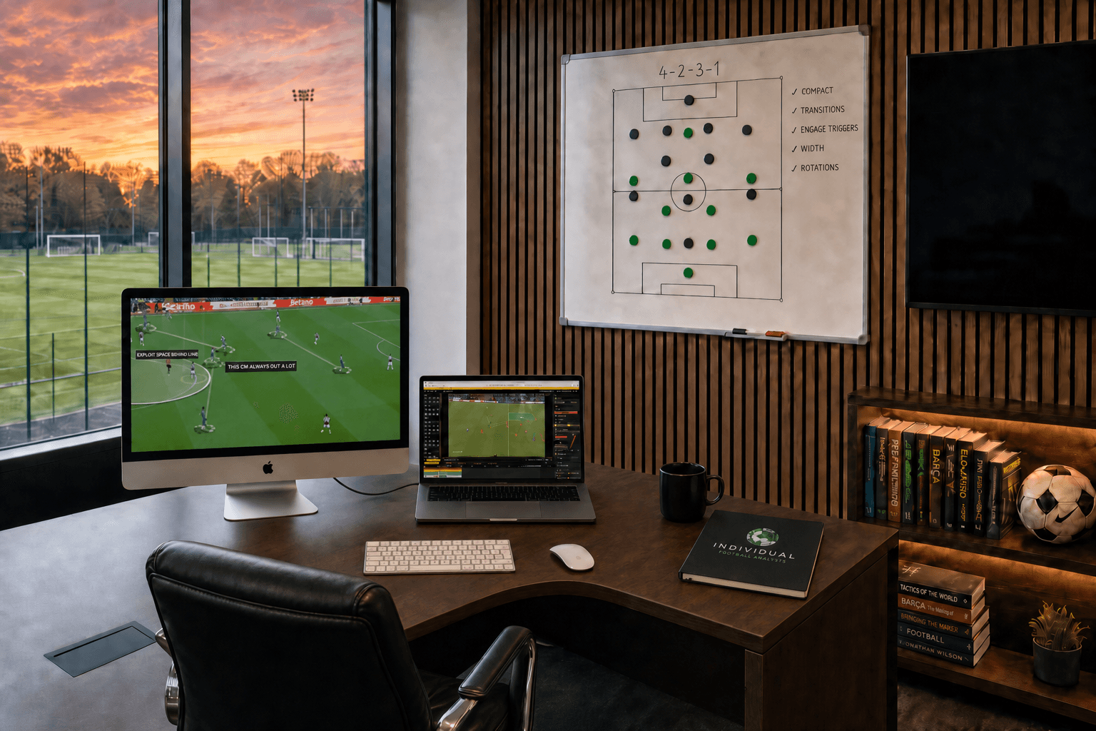 Analysis office with MacBook, dual monitors showing match analysis, tactics board, and training ground pitches through the windows